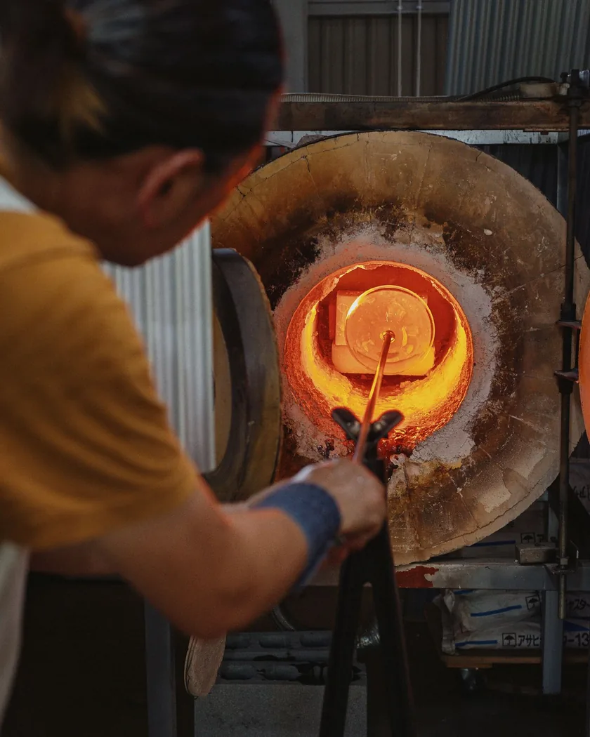 Boca abierta del horno de recalentar con el interior incandescente mientras se introduce una pieza de vidrio montada en la caña